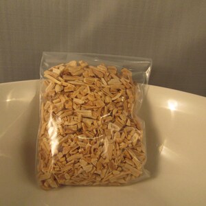 May include: A clear plastic bag filled with light brown wood chips. The bag is sitting in a white bowl. The wood chips appear to be small, rectangular pieces, likely for smoking or grilling.