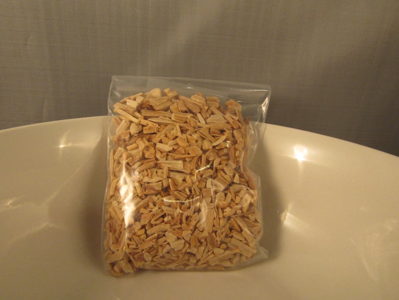 May include: A clear plastic bag filled with light brown wood chips. The bag is sitting in a white bowl. The wood chips appear to be small, rectangular pieces, likely for smoking or grilling.