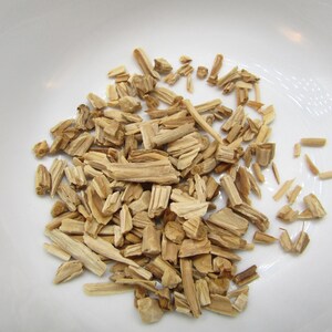 May include: A close-up shot of a white bowl filled with light brown wood chips. The chips are of varying sizes and shapes, with a natural wood grain texture. The bowl is plain and white, providing a clean backdrop for the wood chips.