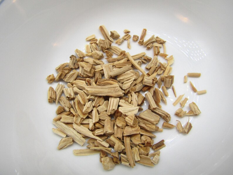 May include: A close-up shot of a white bowl filled with light brown wood chips. The chips are of varying sizes and shapes, with a natural wood grain texture. The bowl is plain and white, providing a clean backdrop for the wood chips.