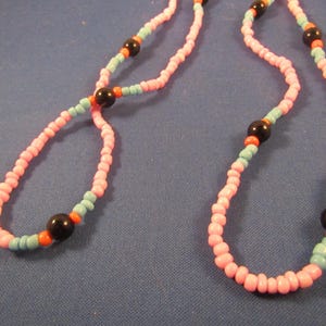 May include: A pink and blue beaded necklace with black and orange accents. The necklace is made of small, round beads and has a simple design.