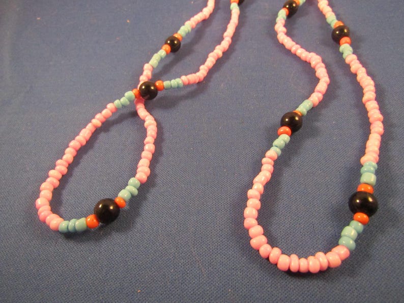 May include: A pink and blue beaded necklace with black and orange accents. The necklace is made of small, round beads and has a simple design.