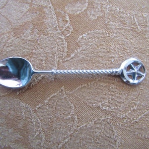 May include: A silver teaspoon with a twisted handle and a crescent moon and star design on the end.