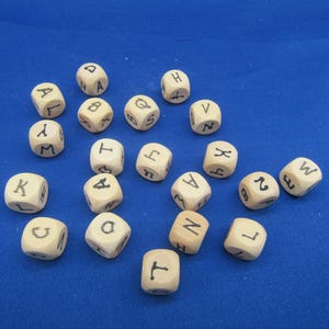 Peut inclure: Un ensemble de dés en bois avec des lettres noires. Les dés sont éparpillés sur une surface bleue.