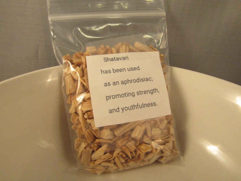 May include: A clear plastic bag filled with light brown, wood-like pieces. A white label on the bag reads "Shatavari has been used as an aphrodisiac; promoting strength, and youthfulness."