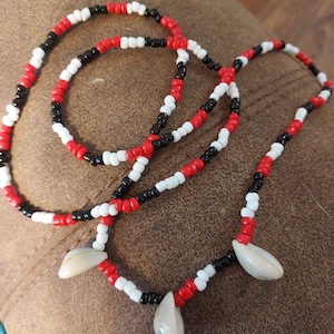 May include: A beaded necklace with black, white and red beads. The necklace has three shell charms attached to it.