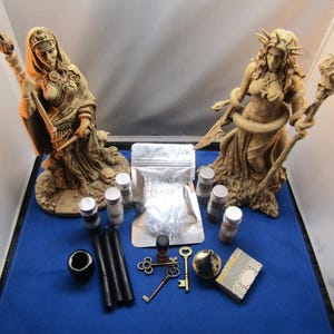 May include: A set of witchy items including two statues of women, a bag of incense labeled "Hecate Incense", small bottles of essential oils, two black candles, a metal incense burner, two keys, and a small wooden box.