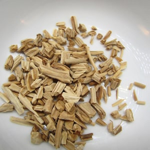 May include: A close-up shot of wood chips, varying in size and shape, scattered across a white surface. The chips are primarily light brown with some darker streaks, suggesting different wood types. Ideal for smoking or grilling.