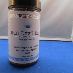 May include: A cylindrical glass jar of incense powder with a black lid. The label reads "Run Devil Run" and "Incense Powder." It also states the product's purpose: "Banish negativity + dispel evil + protect against harm." The jar contains 50gm (1.76 oz.) of powder.