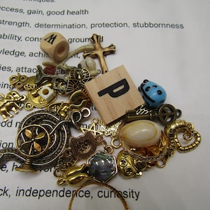 May include: A collection of small, decorative charms and trinkets in gold, bronze, and blue. Includes a wooden die, a cross, a wooden tile with the letter "P", a blue bead, and various other ornate pendants.