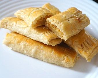 以下が含まれることがあります： 白い皿の上に、金色の焼き菓子が4つ重ねられています。焼き菓子は、明るい色の詰め物で満たされています。