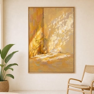 Op de afbeelding: Een abstract olieverfschilderij in een houten lijst toont een zonnige interieurscène. Het kunstwerk heeft een warm kleurenpalet van geel en oranje, met een vaas en schaduwen. De kamer omvat een rieten stoel, een ronde houten tafel en een potplant.