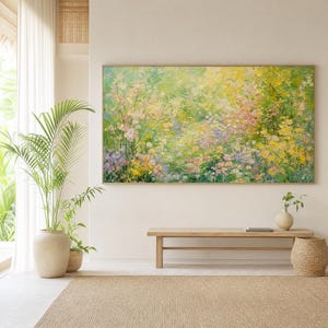 Op de afbeelding: Een groot rechthoekig olieverfschilderij met een impressionistische tuinscène met dikke, getextureerde penseelstreken in tinten geel, groen, wit en zachtroze. Het kunstwerk is ingelijst in een dunne, lichtgekleurde houten lijst.