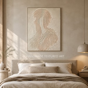 Op de afbeelding: Een rechthoekig wandkunstwerk met een beige, getextureerd oppervlak met verhoogde, gebogen, parallelle lijnen die een abstracte vorm vormen. Het kunstwerk bevat de tekst HANDMADE TEXTURED ART.