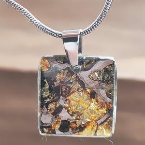 May include: Square pendant with a silver bail and chain. The pendant features a mosaic of gold, brown, and black crystalline structures. The necklace is a unique piece of jewelry.