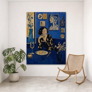 Op de afbeelding: Olieverfschilderij van een vrouw aan een tafel met een wijnglas. Het kunstwerk is in blauwtinten, met gele accenten. Een vaas met bloemen en een wijnglas staan op tafel. Een rotan schommelstoel staat in de buurt.