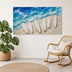 May include: A rectangular wall art piece featuring an oil painting of five white surfboards resting on a sandy beach shore. The ocean waves are depicted in thick, textured strokes of deep blue, turquoise, and white foam along the coastline.