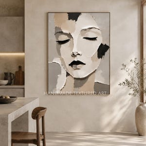 Op de afbeelding: Een rechthoekig wandpaneel met een abstract portret van een gezicht met gesloten ogen in een dikke impasto-stijl. Het kunstwerk gebruikt een neutraal palet van beige, crème, grijs en zwarte tinten met zichtbare verftextuur en de tekst HANDMADE TEXTURED ART.