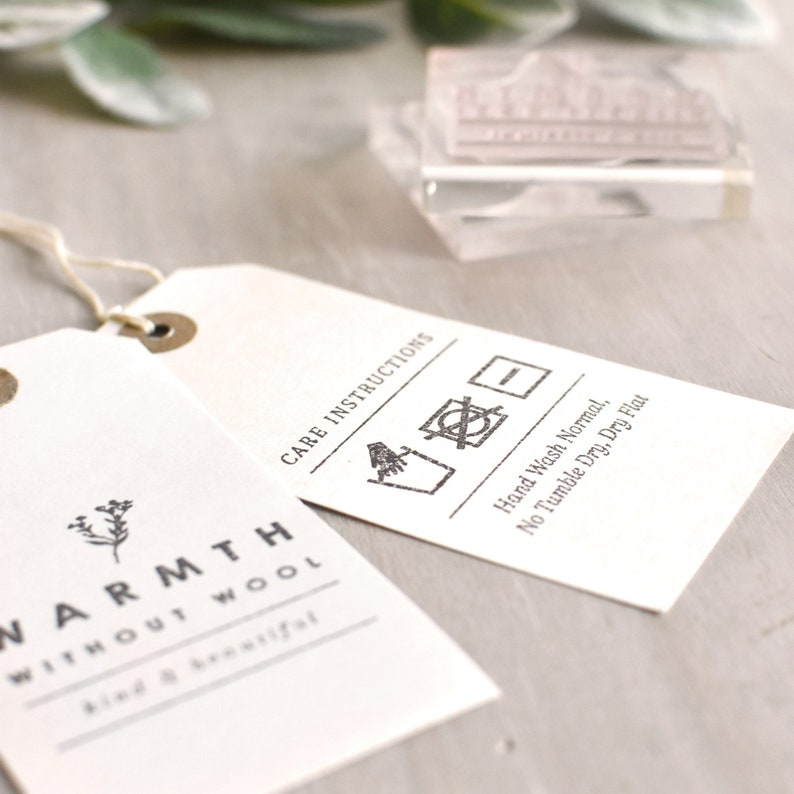 Puede incluir: Una etiqueta blanca con texto negro que dice "WARMTH WITHOUT WOOL kind & beautiful" y "CARE INSTRUCTIONS". La etiqueta tambi&eacute;n incluye un s&iacute;mbolo de cuidado de la ropa en blanco y negro para lavar a mano, no secar en secadora y secar en plano.
