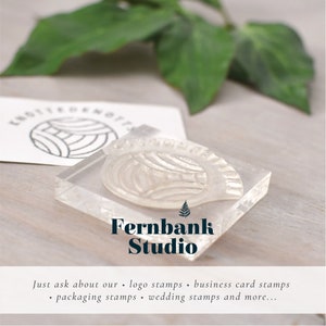 Puede incluir: Un sello de acr&iacute;lico transparente con un dise&ntilde;o de hoja de helecho. El sello est&aacute; etiquetado como "Fernbank Studio". El texto "Just ask about our logo stamps, business card stamps, packaging stamps, wedding stamps and more..." est&aacute; debajo del sello.