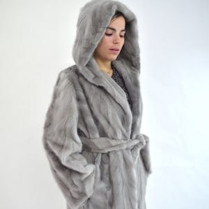 Real sapphire mink fur coat with hood and belt. Genuine mink stroller in gray, unique jacket from premium mink skins, farming fur pelts.