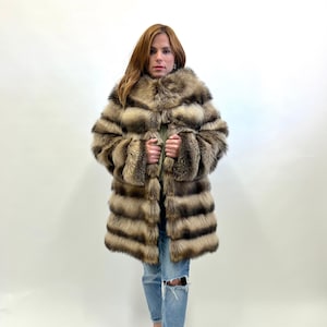 May include: A brown and black striped fur coat with a large collar. The coat is worn by a person with long brown hair and is paired with blue jeans and black shoes.