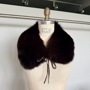 May include: A dark brown fur collar with a tie closure, displayed on a vintage dress form. The collar is plush and appears to be made of fox fur. The dress form has the text "ROYAL FORM" printed on it.