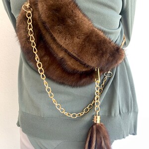 May include: A brown fur crossbody bag with a gold chain strap and a brown fur tassel.