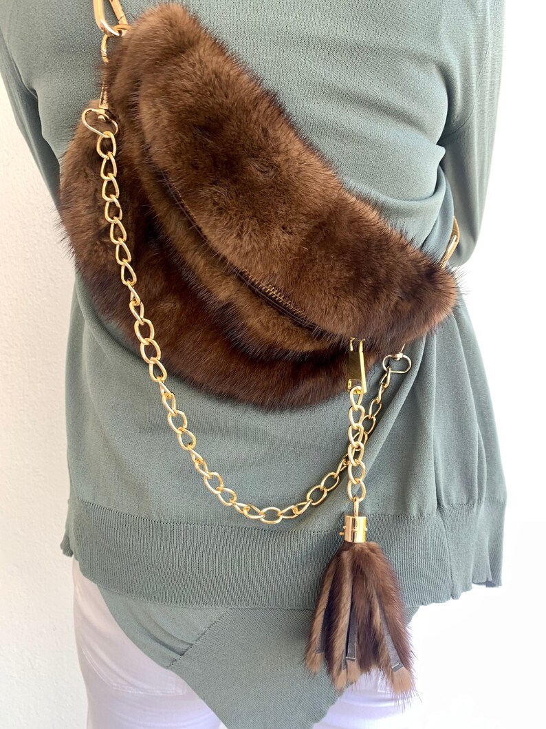 May include: A brown fur crossbody bag with a gold chain strap and a brown fur tassel.