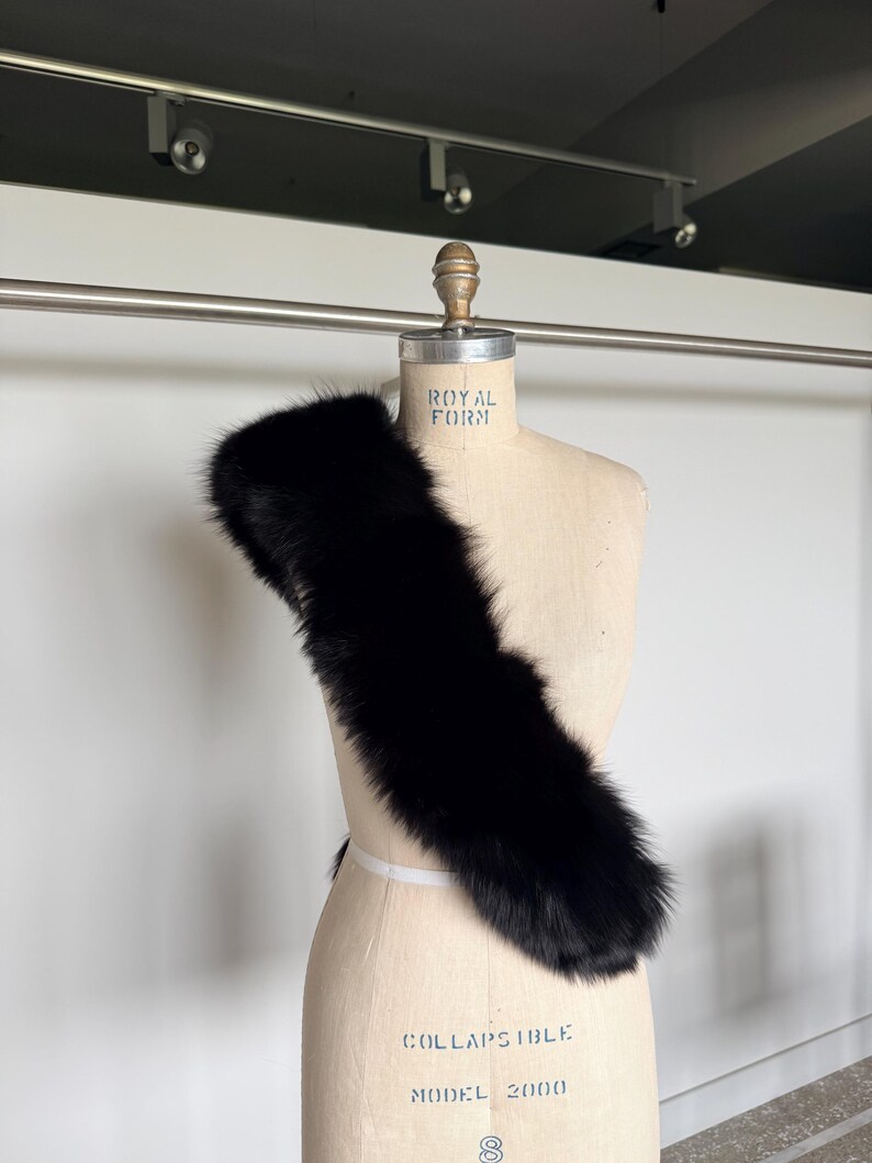 May include: A black fur stole draped over a mannequin. The stole is made of soft, dark fur and is displayed on a vintage-style mannequin with the text "Royal Form" and "Collapsible Model 2000".