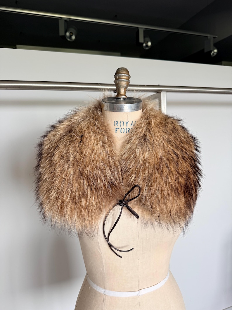 Op de afbeelding: Een luxe bontkraag met bruine en zwarte tinten. De kraag wordt getoond op een mannequin en heeft een donkerbruine striksluiting. De tekst "ROYAL FOR" is zichtbaar op de mannequin.
