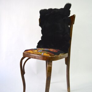 May include: A wooden chair with a black fur cushion on the seat. The chair has a curved back and four legs. The seat is covered in a colorful fabric with a floral pattern.