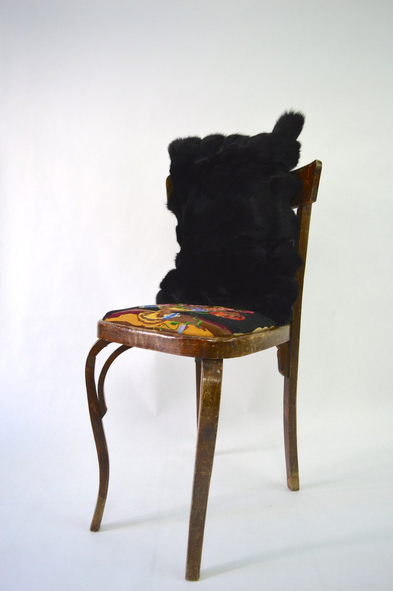 May include: A wooden chair with a black fur cushion on the seat. The chair has a curved back and four legs. The seat is covered in a colorful fabric with a floral pattern.
