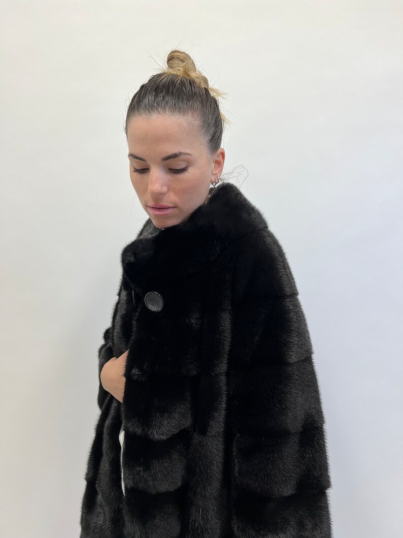 May include: A black fur coat with a button fastening. The coat is made from a soft, luxurious fur and has a classic, elegant style.