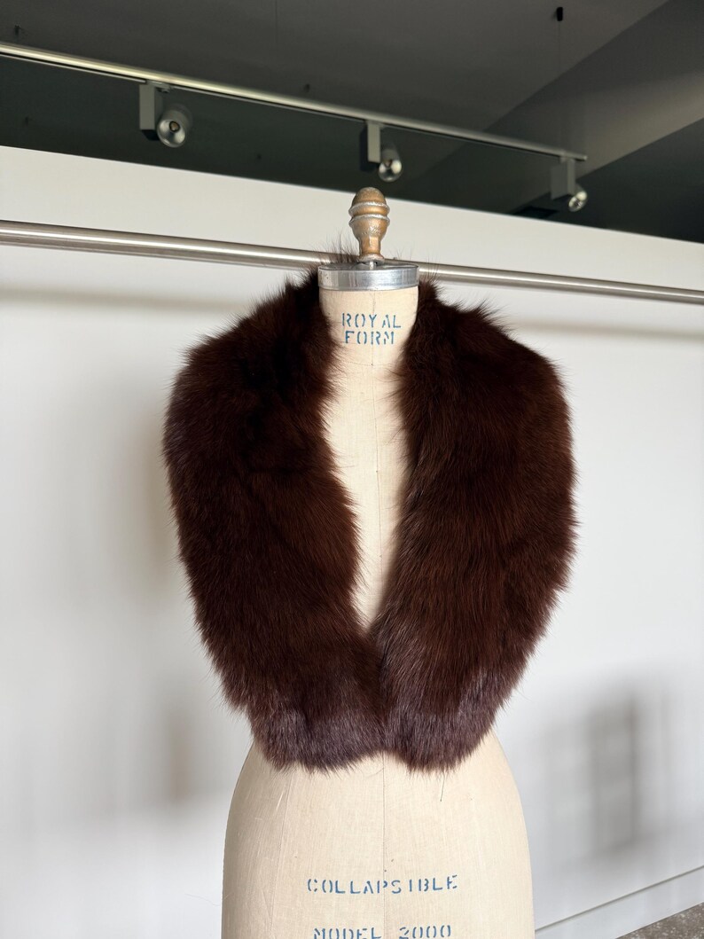 May include: A luxurious brown fur collar displayed on a vintage dress form. The collar is a rich, dark brown color, with a soft, plush texture. The dress form has the text "ROYAL FORM" printed on it.