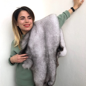 Puede incluir: Una mujer sostiene una piel de zorro plateado. La piel es suave y esponjosa, con una capa interna gris oscura. La piel es grande y lujosa.