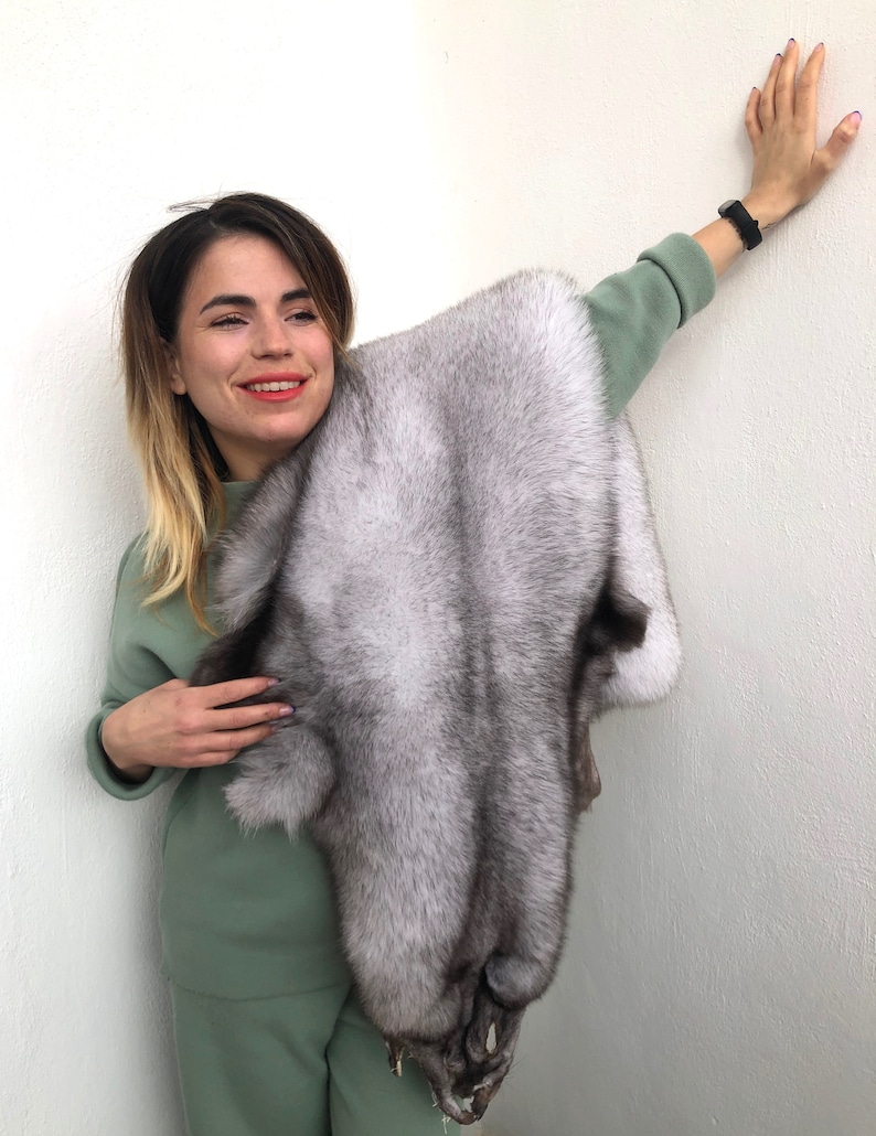 Puede incluir: Una mujer sostiene una piel de zorro plateado. La piel es suave y esponjosa, con una capa interna gris oscura. La piel es grande y lujosa.