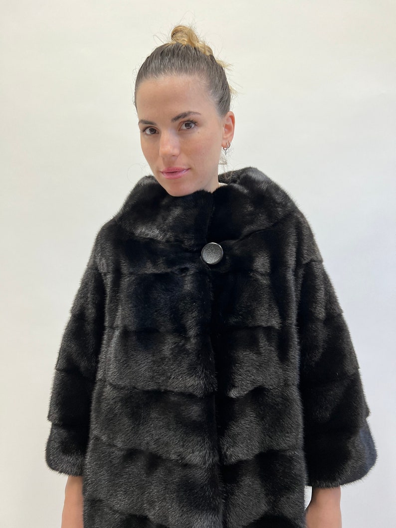May include: A black fur coat with a single button fastening. The coat has a collar and is made of a soft, luxurious fur.