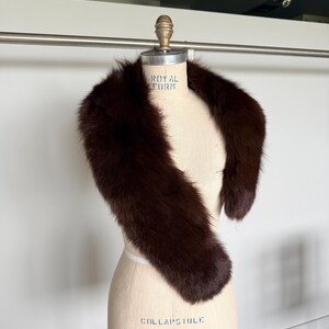 May include: A dark brown fur stole draped over a dress form. The stole is a rich, deep brown color and appears soft and luxurious. The dress form is a light beige color, with text that reads "ROYAL FORM" and "COLLAPSIBLE MODEL 2000".