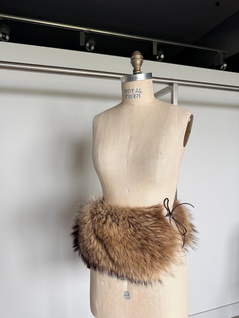 Op de afbeelding: Een bruine bontkraag met een donkerbruine striksluiting wordt getoond op een vintage paspop. De kraag is gemaakt van zacht, pluizig bont en is ontworpen om om de nek te worden gedragen.