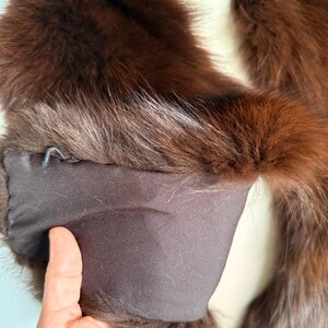 May include: A luxurious brown fur stole with a dark brown satin lining. The fur appears to be fox or mink, with a rich, reddish-brown hue. The stole is draped over a mannequin, showcasing its shape and texture.
