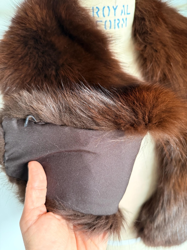 May include: A luxurious brown fur stole with a dark brown satin lining. The fur appears to be fox or mink, with a rich, reddish-brown hue. The stole is draped over a mannequin, showcasing its shape and texture.