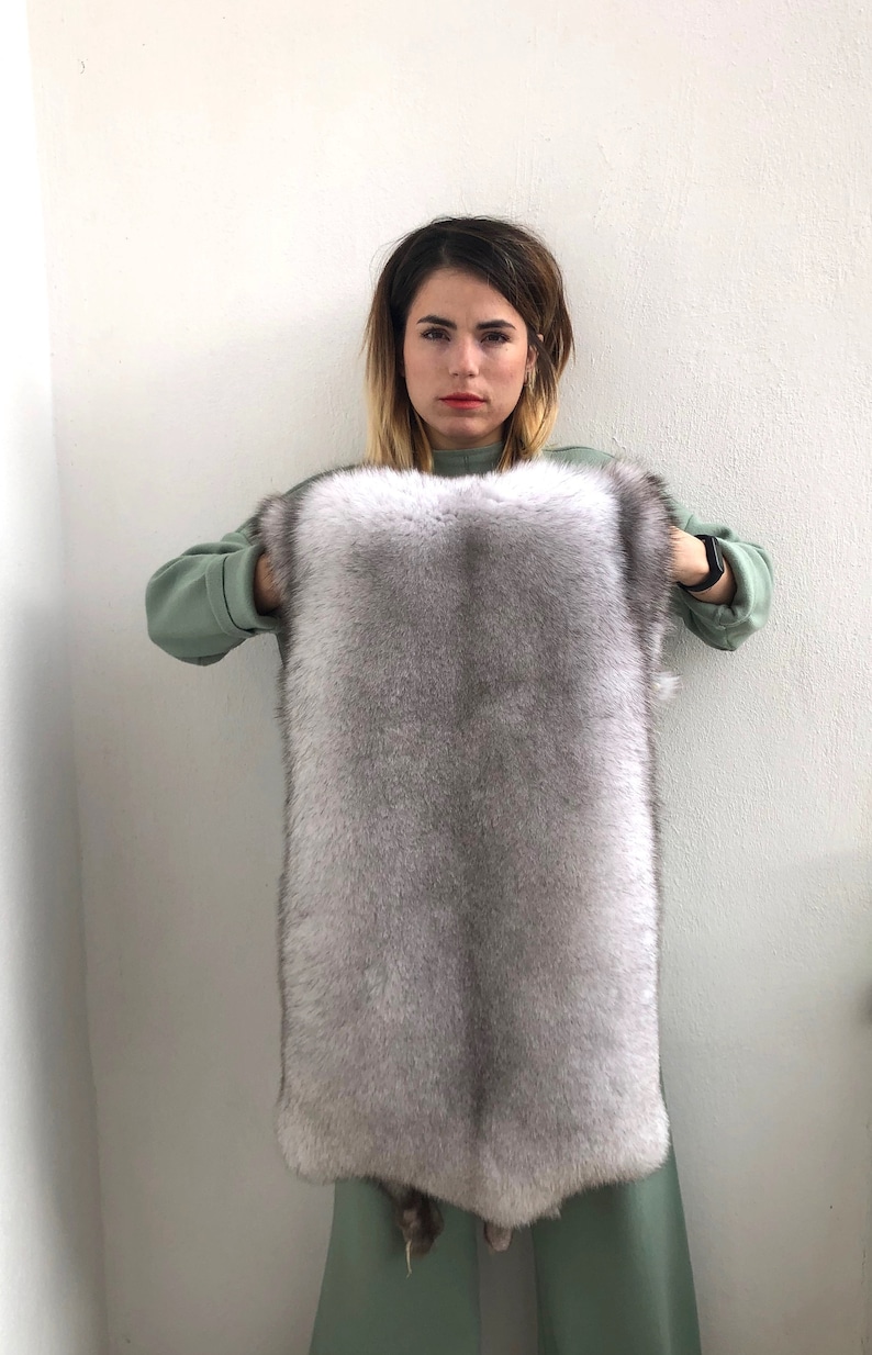 Puede incluir: Una persona sostiene una gran piel de piel gris claro. La piel es suave y esponjosa, y la piel tiene forma rectangular.