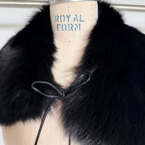 May include: A black fur collar with a leather tie closure. The collar is displayed on a mannequin with the text "ROYAL FORM" printed on it. The fur appears soft and luxurious.