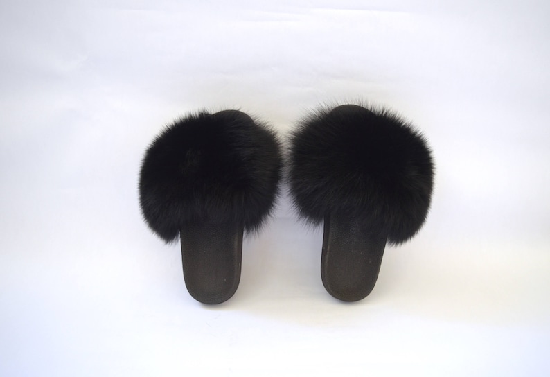 K&ouml;nnte beinhalten: Ein Paar schwarze Fellslipper. Die Slipper haben einen flauschigen schwarzen Pelzbesatz am oberen Rand des Slippes.