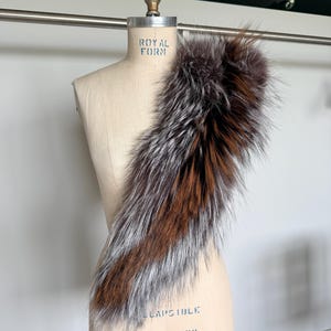 May include: A luxurious fur collar displayed on a mannequin. The collar features a blend of brown, silver, and dark brown fur. The mannequin is a neutral beige color, with the text "ROYAL FORM" and "LAPSBILE MODEL 2000" printed on it.