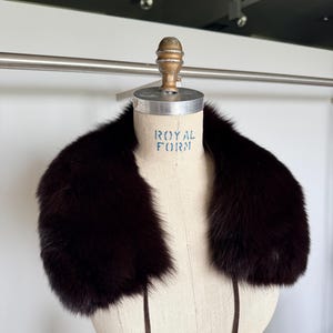 May include: A dark brown fur collar displayed on a mannequin. The collar is thick and plush, with a deep, rich color. The mannequin has the words "ROYAL FORM" printed on it.