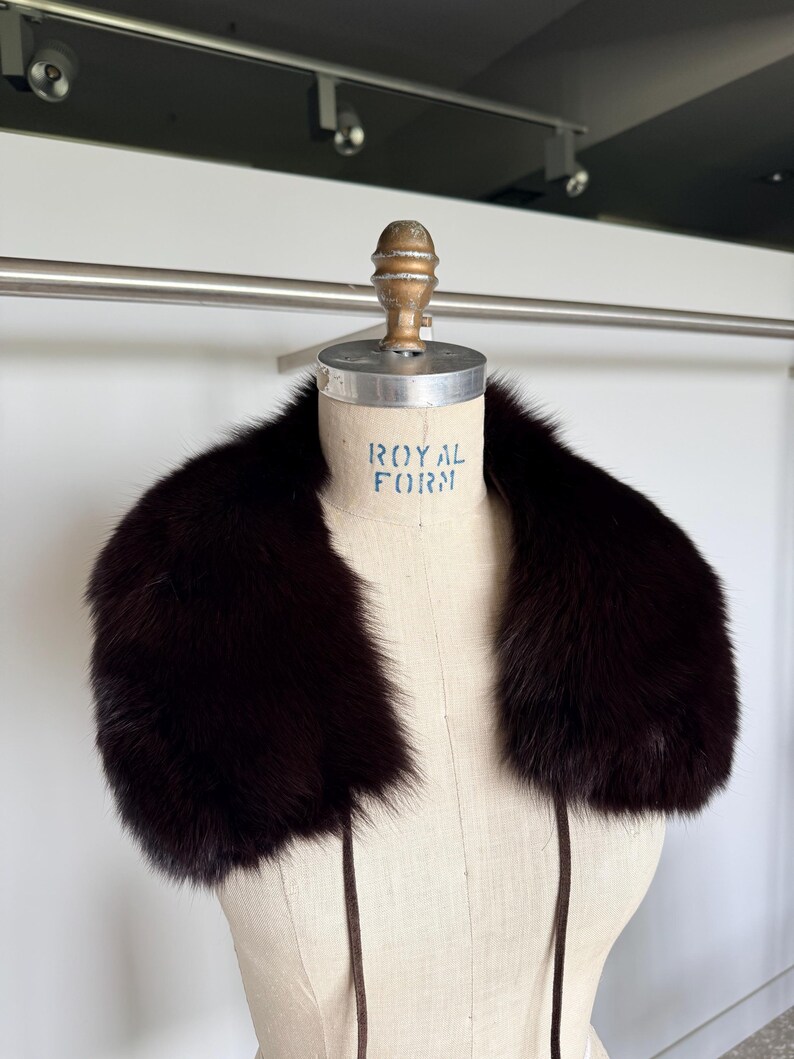 May include: A dark brown fur collar displayed on a mannequin. The collar is thick and plush, with a deep, rich color. The mannequin has the words "ROYAL FORM" printed on it.