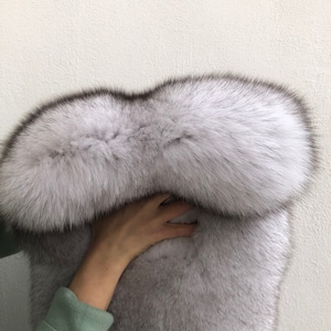 Puede incluir: Una estola de piel gris larga, suave y esponjosa con un cuello grueso y redondeado. La piel es suave y lujosa, y el cuello es muy completo.