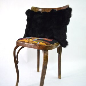 May include: A black faux fur pillow sits on a wooden chair with a colorful floral patterned seat. The chair has a curved back and four legs.